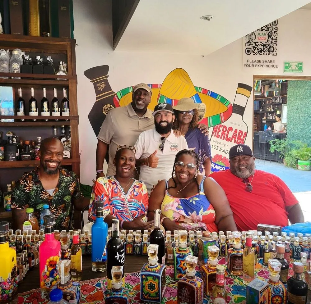 A Juan More Taco guide and smiling guests around a colorful tequila counter in Cabo San Lucas