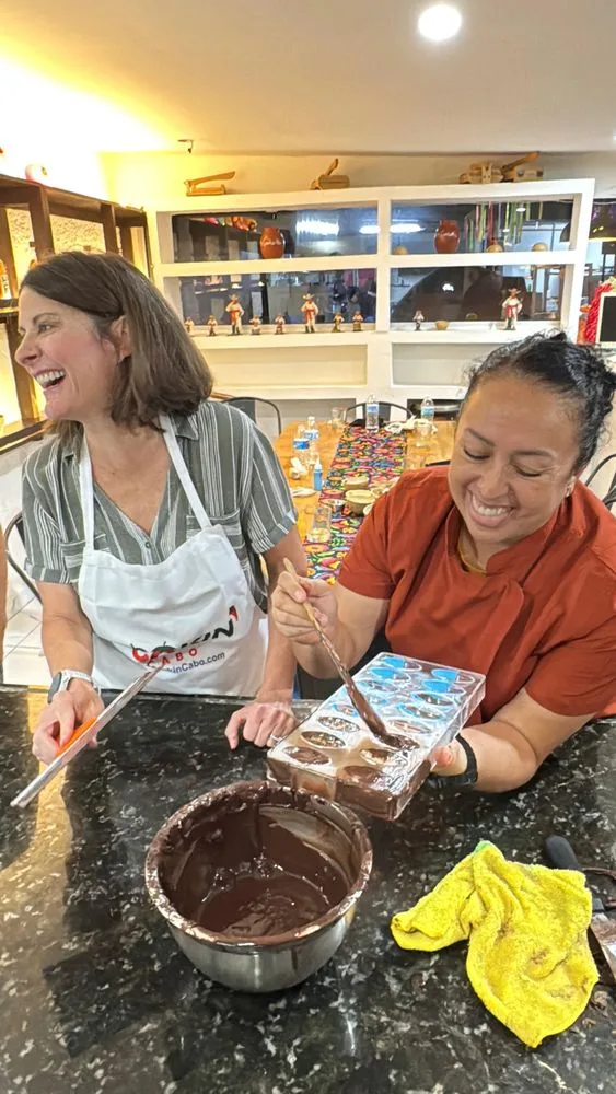 Two smiling guests filling chocolate molds during a hands-on Cabo San Lucas cacao workshop