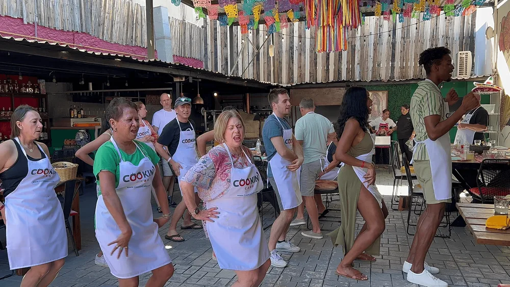 Guests in cooking aprons learning Latino dance steps at an open-air Cabo San Lucas class